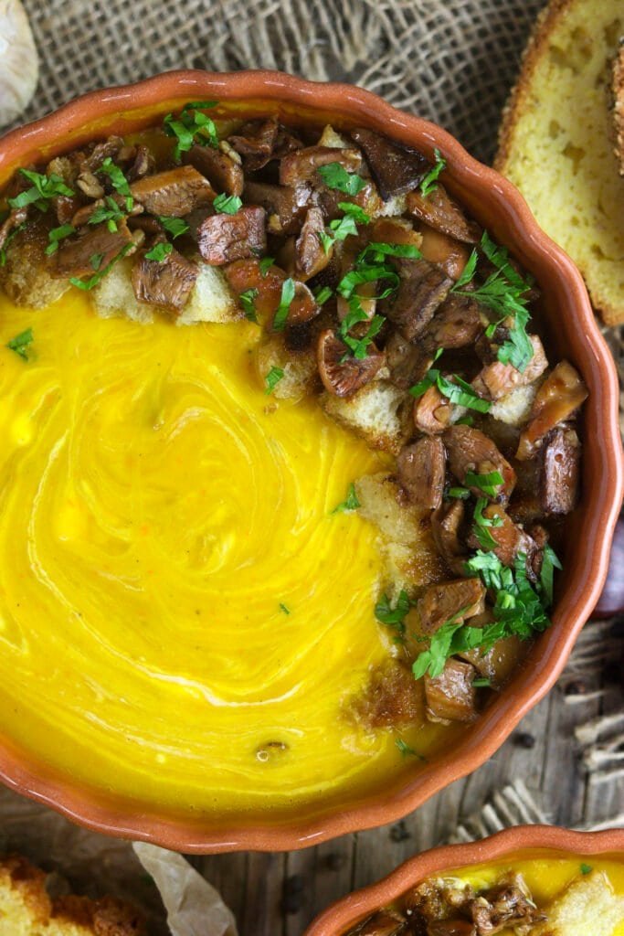 Top view of a mushroom squash soup in a bowl with sautéed saffron milk caps and bread croutons on top.