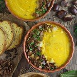 A close top shot of mushroom squash soup with saffron milk cap mushrooms, bread croutons and fresh parsley on top. Bread, garlic and chestnut in the background.