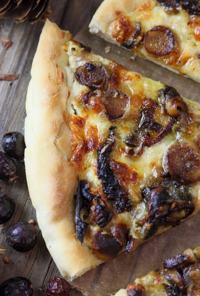 A slice of pizza with porcini mushrooms on a wooden table, with melted cheese and fried porcini mushrooms visible on top.