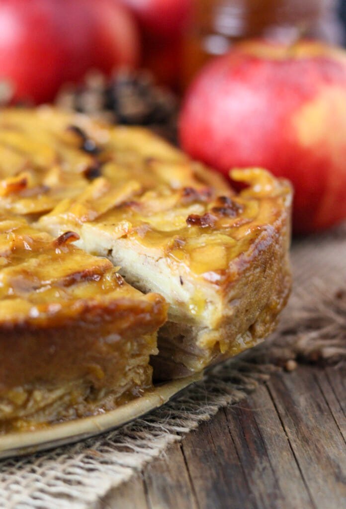 A close view of sliced buckwheat cake with apples and honey, with red apples in the background.