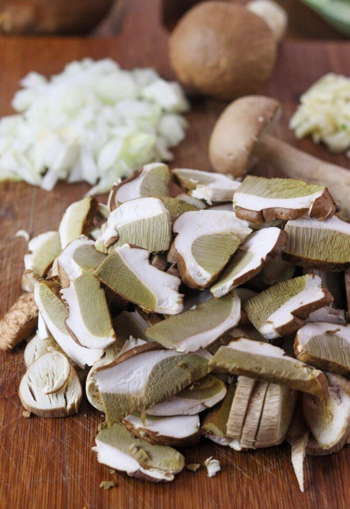 Sliced fresh porcini mushrooms with diced onion, garlic and baby porcini in the background.