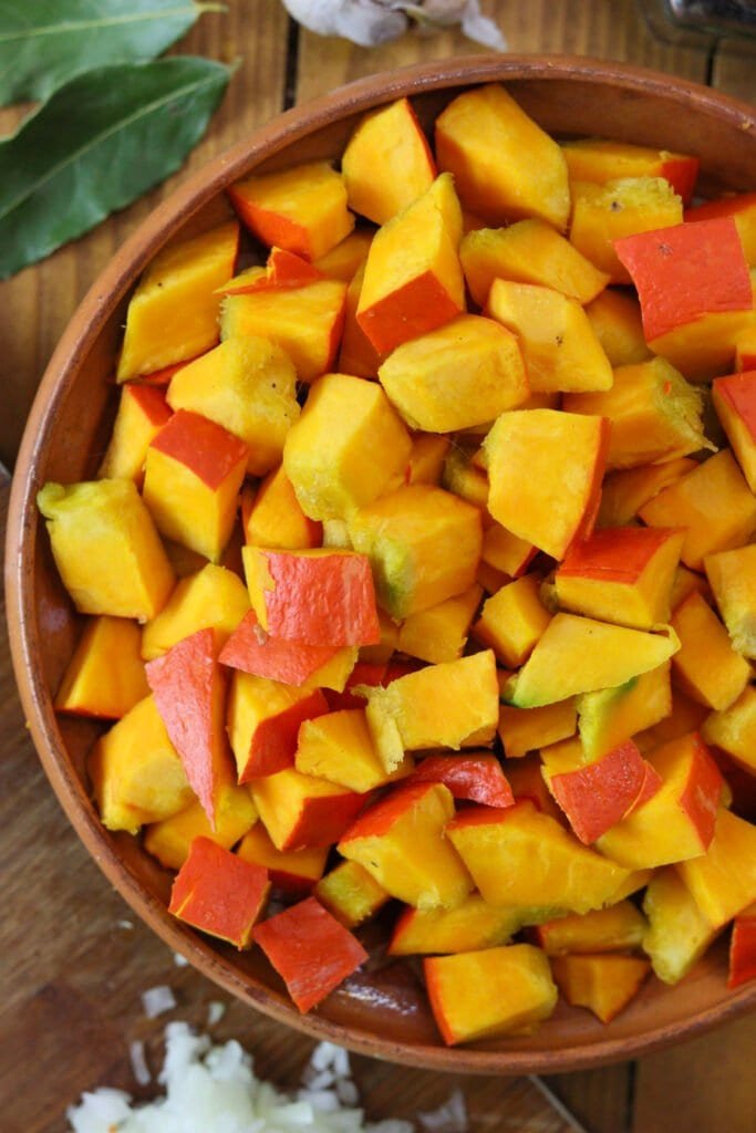 Diced kuri squash in a bowl with bay leaves in the background