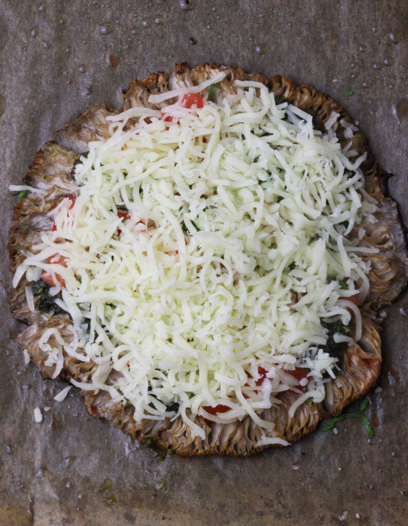 Mushroom being topped with shredded mozzarella cheese.