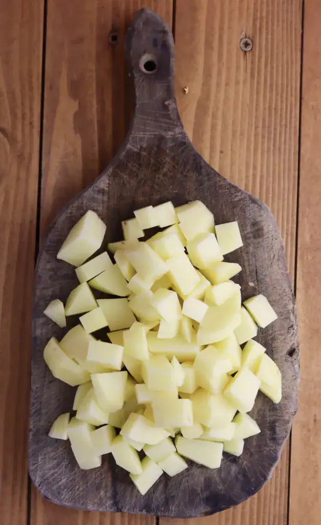 pealing the potatoes and cutting them into small pieces before adding them to a pot with other ingredients