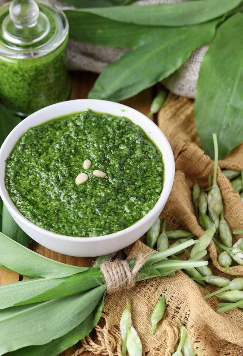 Pesto with wild garlic and toasted pine nuts served in a bowl with wild garlic leaves in the bacground.
