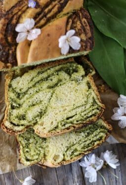 Slices of wild garlic bread with wild garlic leaves and cherry flowers in the background.