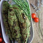 Grilled mackerels, wrapped in fig leaves and grilled with a rosemary sprig and tomato, olive oil and garlic in the background.
