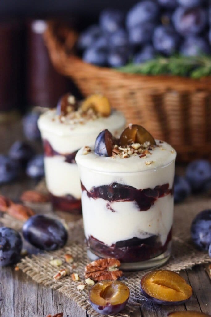 Two cups of plum parfait with white chocolate and fresh plums in front and at the back.