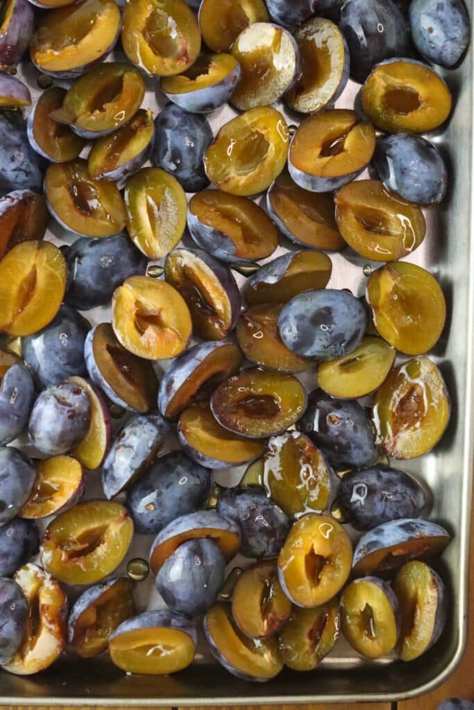 Plum halves placed on a baking tray, drizzled with honey.