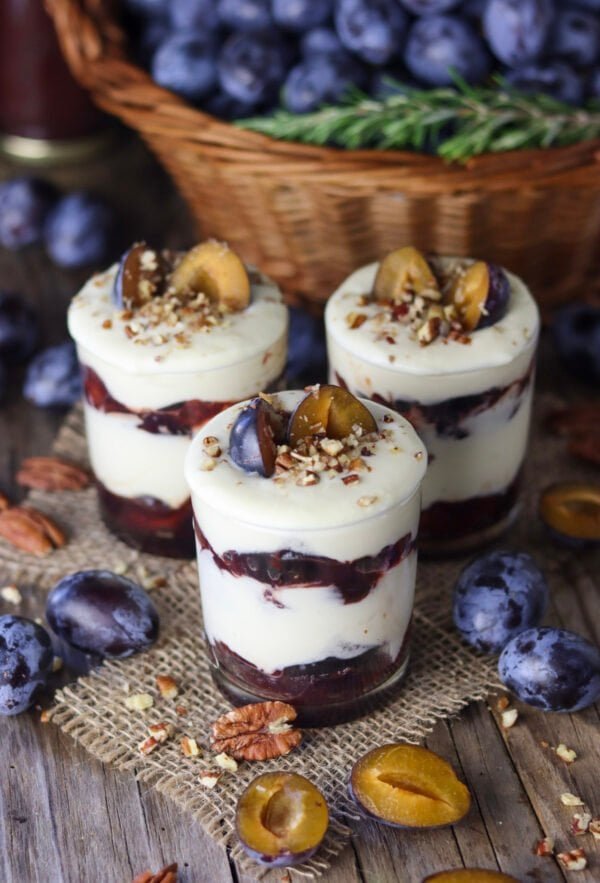 Three jars of roasted plum parfait with white chocolate and plums in the background.